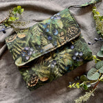 Green patterned pouch with nature-themed design on a textured fabric background