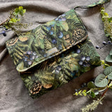 Green patterned pouch with nature-themed design on a textured fabric background