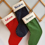 personalized Christmas stockings in red, blue, and green with names embroidered on them.