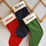 personalized Christmas stockings in red, blue, and green with names embroidered on them.