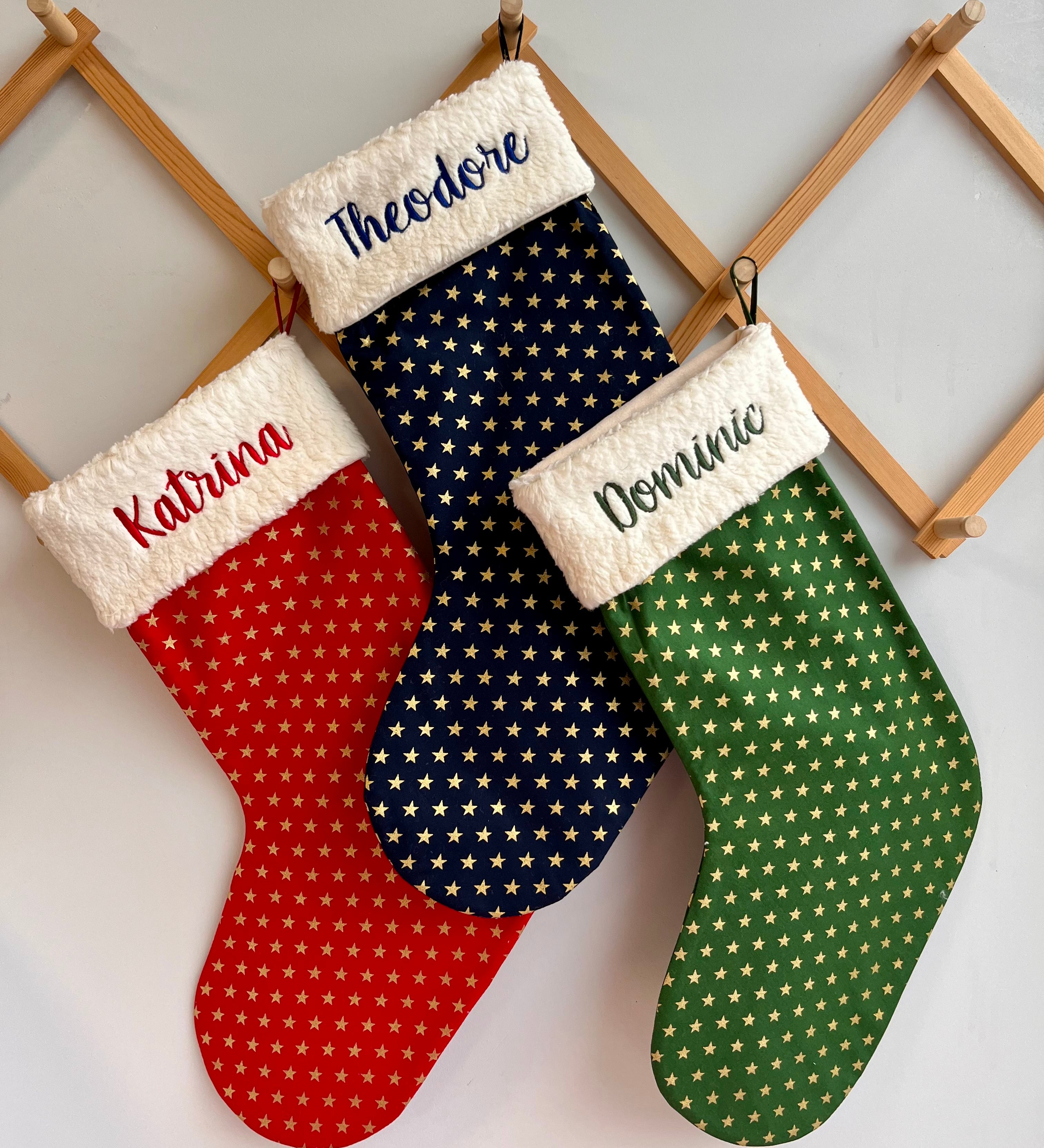 personalized Christmas stockings in red, blue, and green with names embroidered on them.