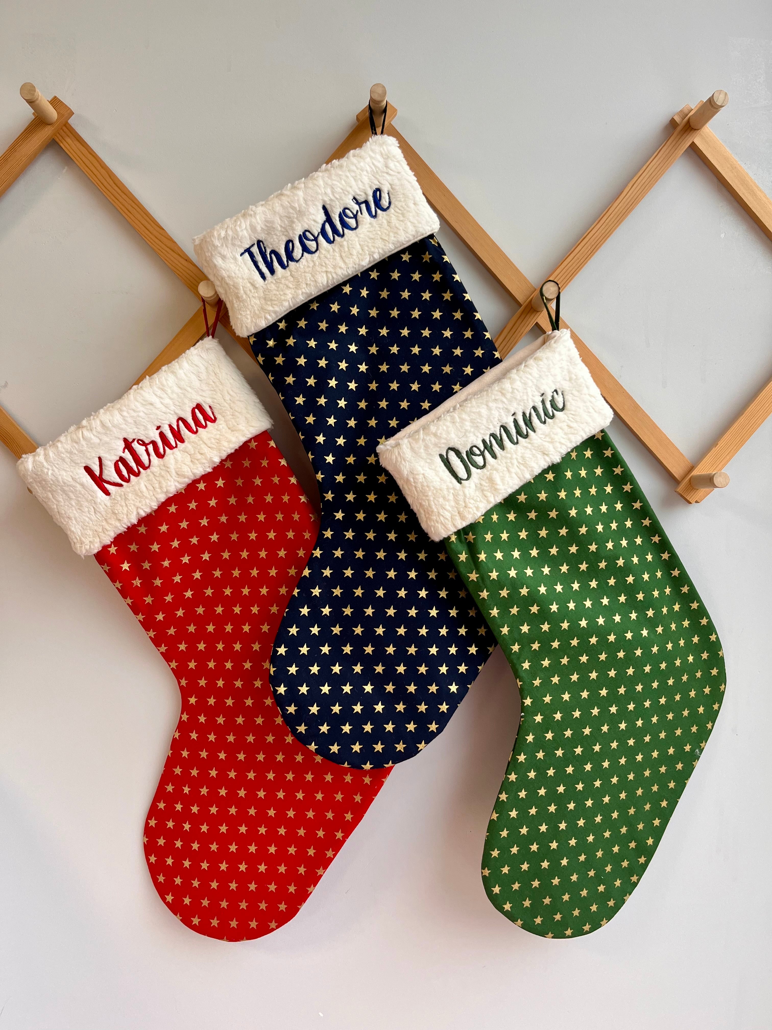 personalized Christmas stockings in red, blue, and green with names embroidered on them.