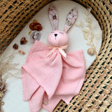 Pink bunny plush toy with a blanket on a textured surface