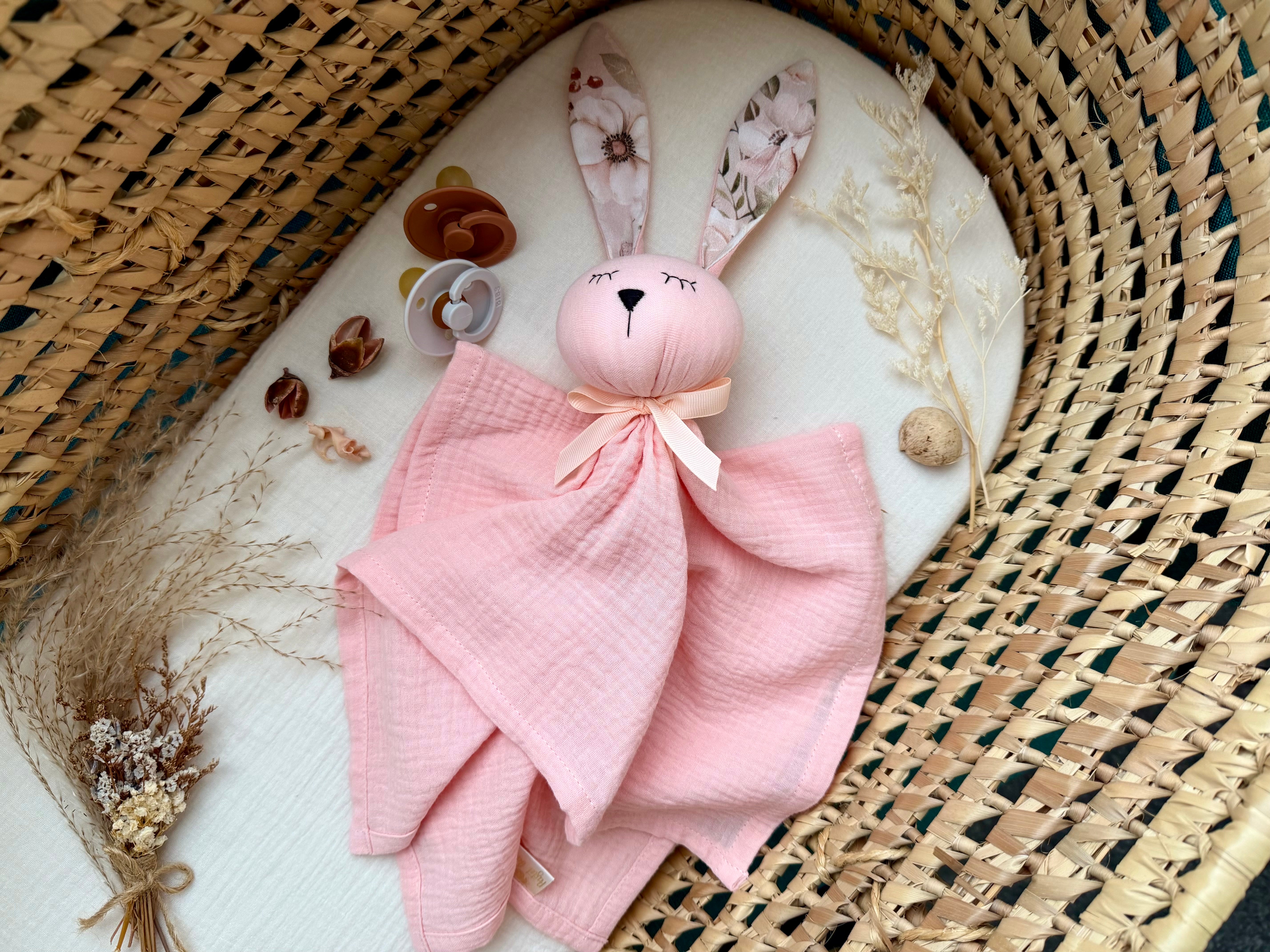 Pink bunny plush toy with a blanket on a textured surface