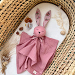 Pink plush toy with bunny ears on a white surface with a wicker basket in the background